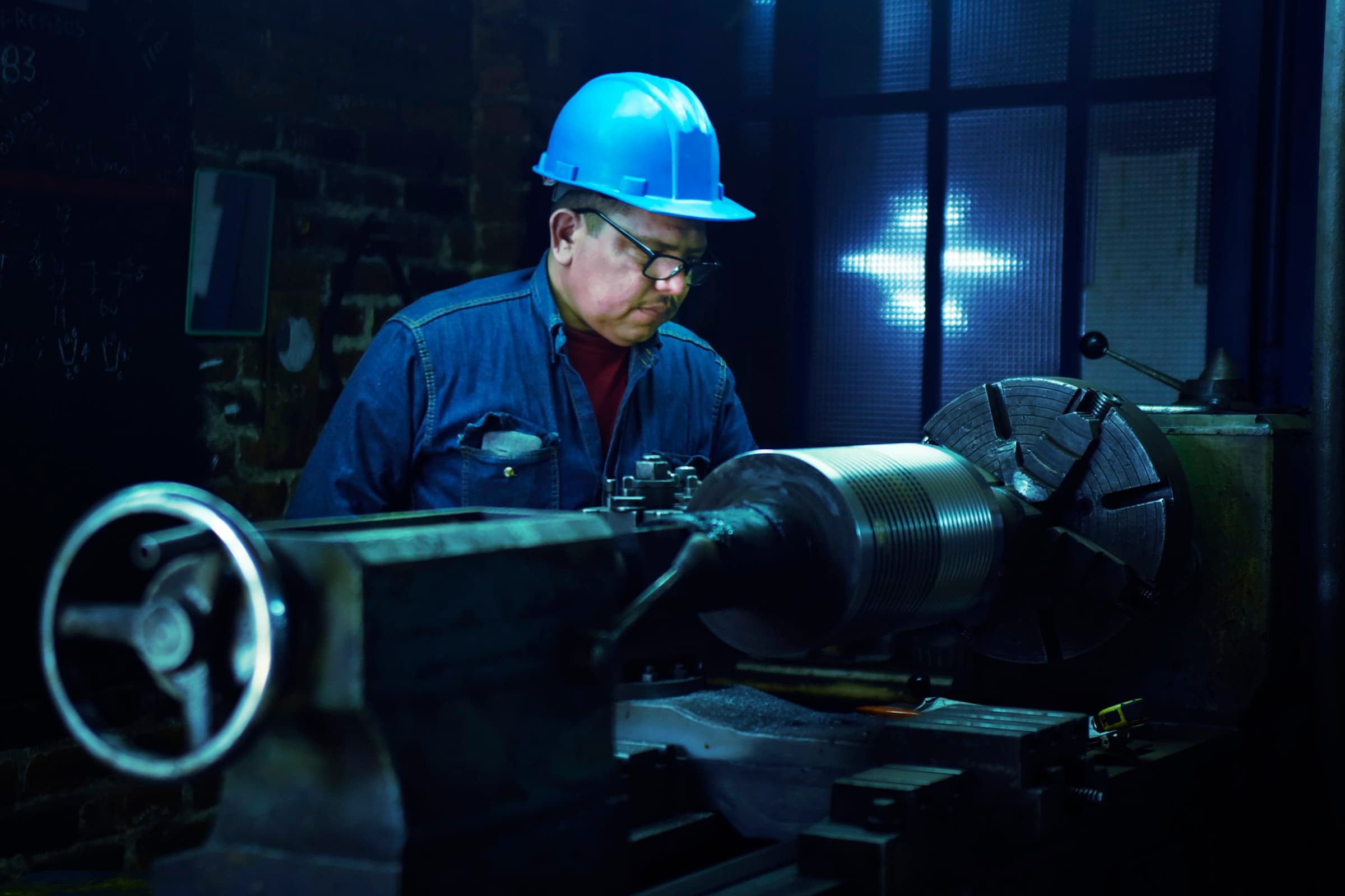Machinist in a hard hat running a lathe